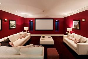 a cinema room in an expensive new home with large comfortable cream coloured settees, silk cushions and a foot stool. On either side of the screen are recessed windows with electronic blinds (lowered) and alcove lights. The pictures on the wall are the photographer's.